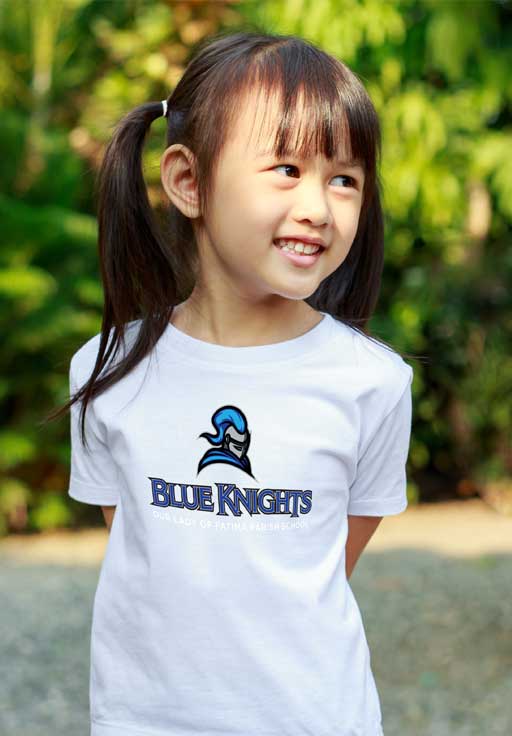 A young girl poses in an outdoor park0like setting wearing a Blue Knights t-shirt.