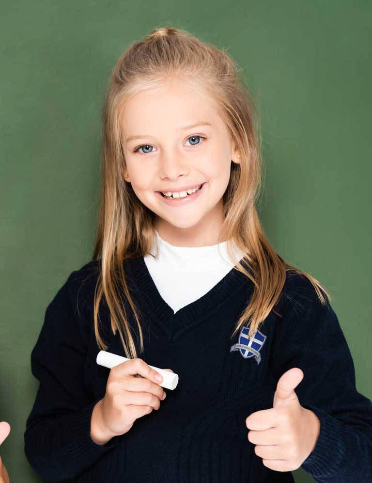 A young girl wearing a new Our Lady of Fatima uniform poses against a chalkboard.