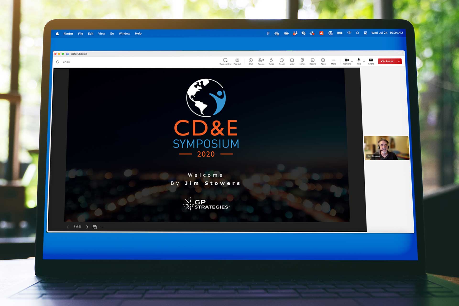 Laptop screen displays title slide that says, "CD&E Symposium 2020," Welcome by Jim Stowers.