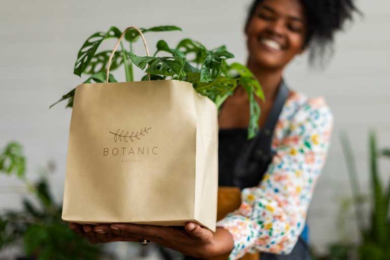 Woman holding brown bag of plants with logo printed on bag.